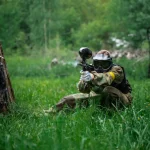 The player shoots a gun on the battlefield in a paintball