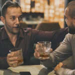 Deux amis masculins passant du temps ensemble dans un bar ou un pub. Hommes adultes tenant des verres de whisky ou de brandy. Des amis communiquent et discutent avec des verres en cristal dans les mains.